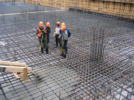 Five workers are standing on the foundation of concrete reinforcing mesh.